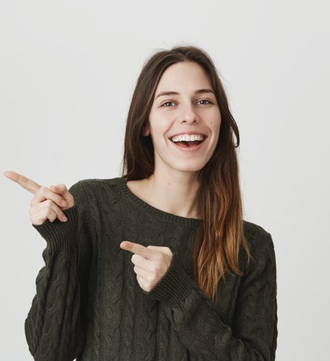 Advertising concept. Excited cheerful european woman wearing casual clothes smiling and exclaiming, pointing index fingers at copy space on studio wall, motivating and attracting customers. Advertising concept. Excited cheerful european woman wearing casual clothes smiling and exclaiming, pointing index fingers at copy space on studio wall, motivating and attracting customers.